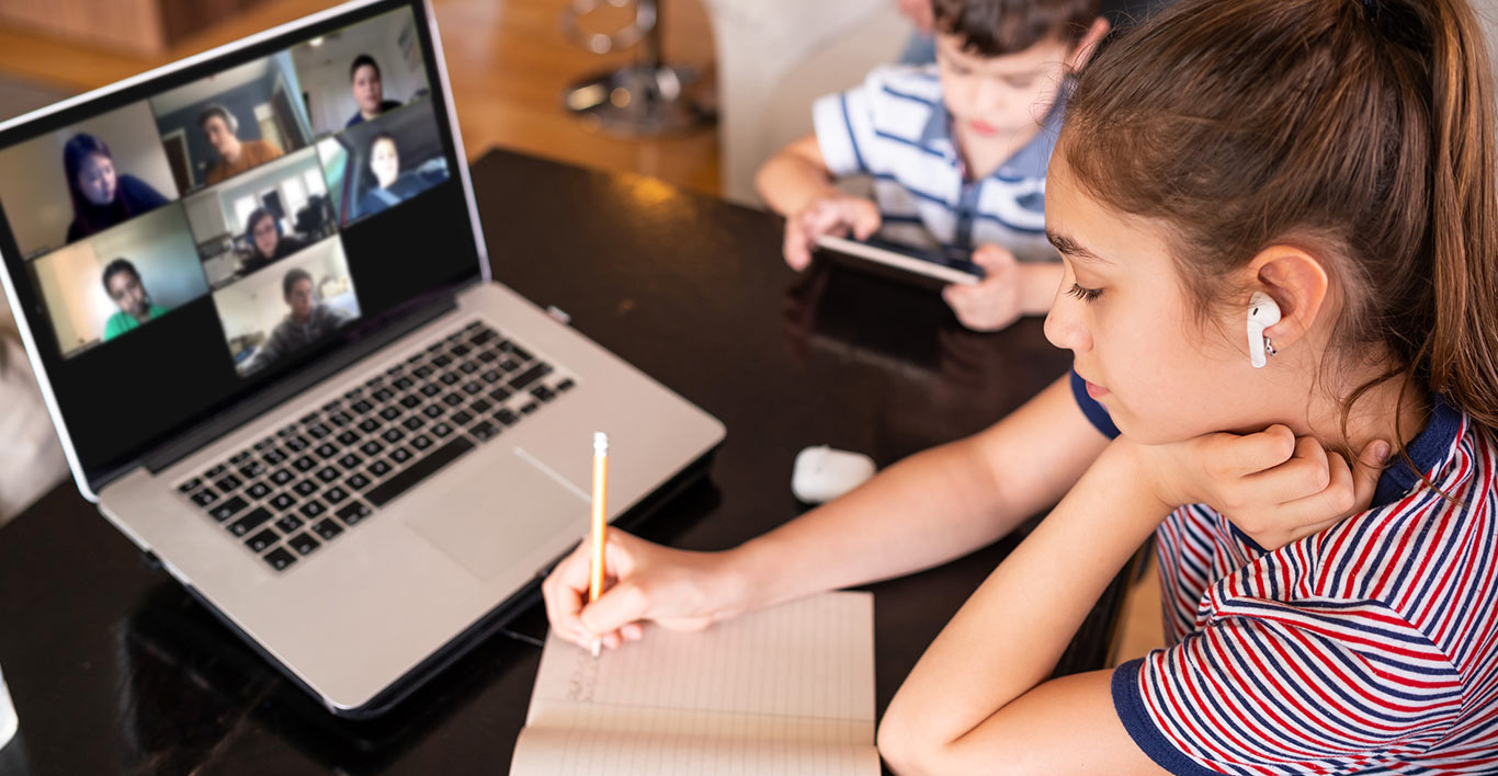 a student takes notes in a paper notebook while sitting in a video call on her laptop